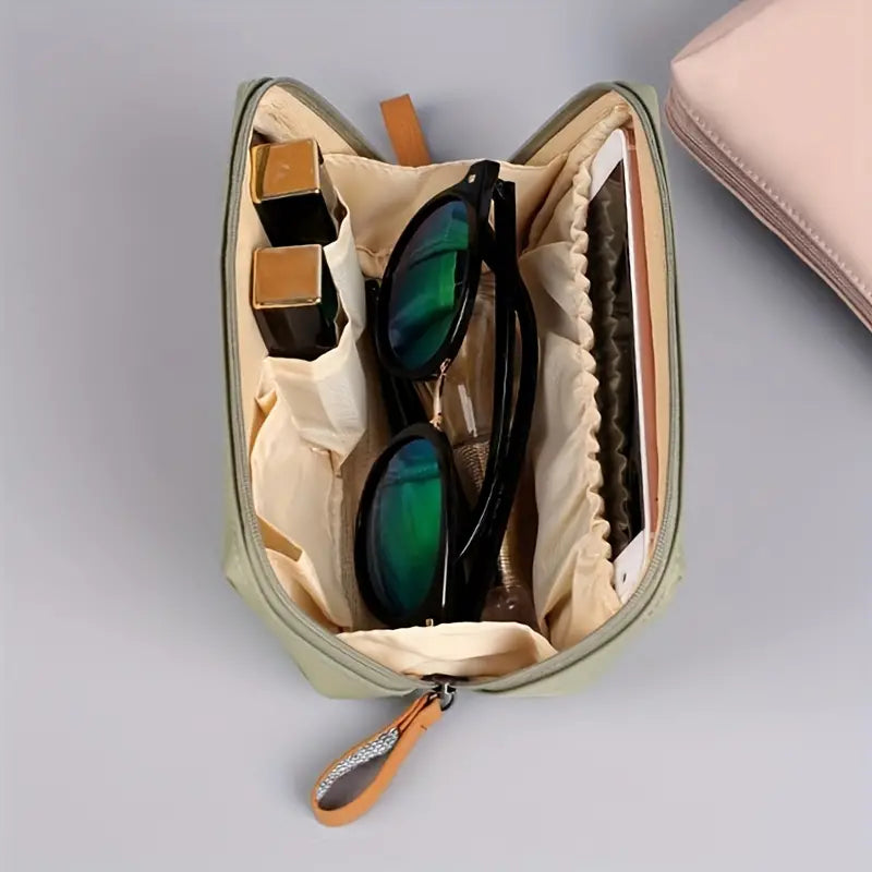 Custodia organizer da viaggio aperta con occhiali da sole, rossetti e smartphone. Design compatto, ideale per accessori e cosmetici.