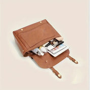 Borsa a tracolla in pelle marrone aperta, contenente smartphone, cosmetici e accessori. Design elegante, ideale per moda e praticità quotidiana.