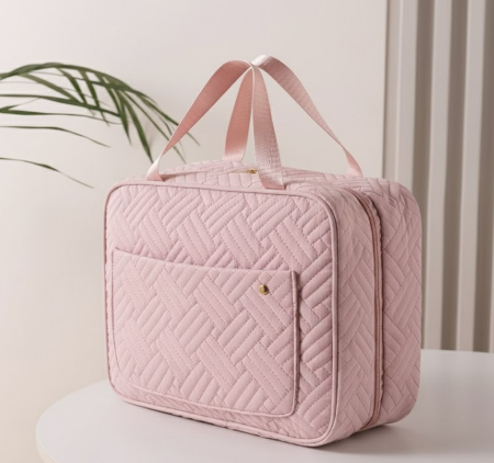 Borsa da viaggio rosa trapuntata su tavolo bianco, con manici e tasca frontale. Design elegante, ideale per organizzare accessori e cosmetici.