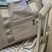 Borsa da viaggio grigia con cerniera su valigia rigida argentata, manico telescopico. Accessori viaggio eleganti, pratici e resistenti.