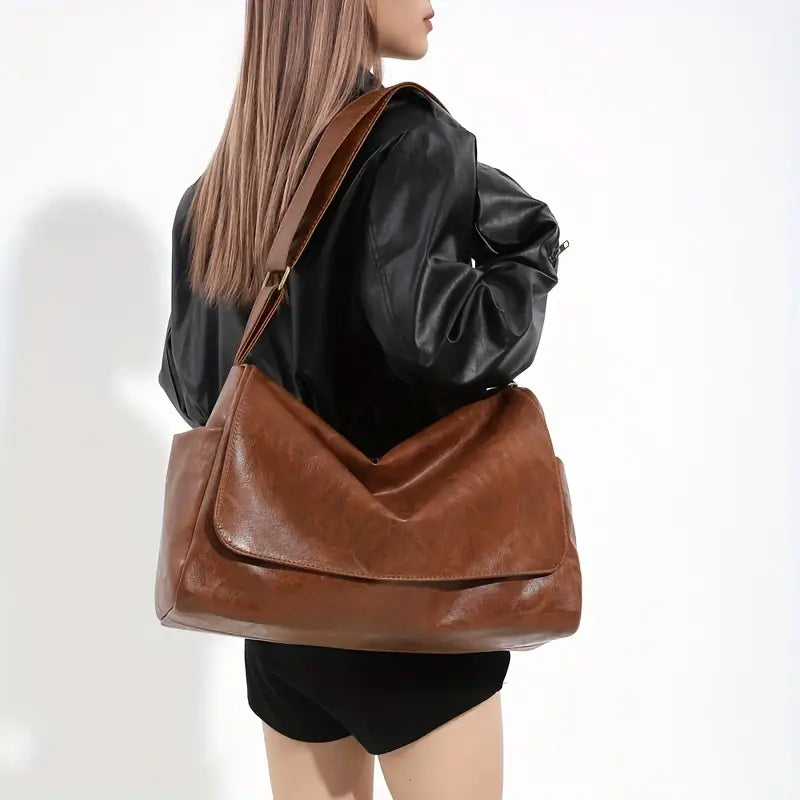 Donna con borsa a tracolla in pelle marrone, giacca nera. Accessorio moda elegante, capiente e versatile per uso quotidiano.