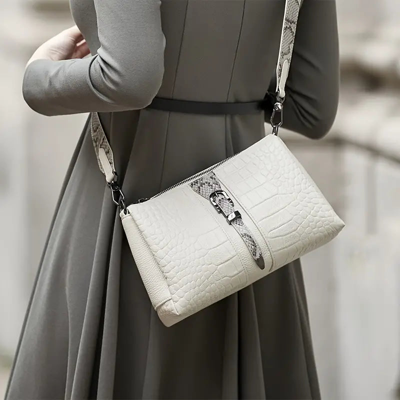 Donna con borsa a tracolla in pelle bianca effetto coccodrillo, abito grigio elegante. Accessorio moda femminile, stile sofisticato.