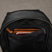 Zaino in pelle nera aperto con portafoglio marrone visibile all'interno. Design elegante, ideale per viaggi e uso quotidiano. Accessori moda uomo.