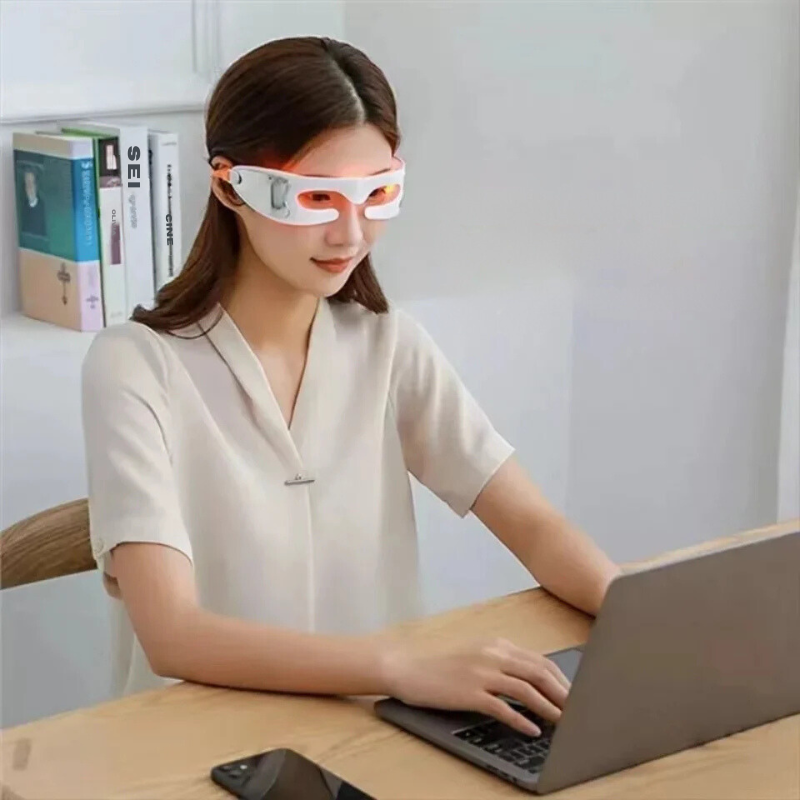 Donna con maschera massaggiante per occhi, seduta al computer portatile. Tecnologia benessere, relax visivo, cura occhi, lavoro da casa.