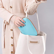 Donna con abito beige inserisce pochette azzurra in borsa bianca. Moda femminile, accessori eleganti, stile casual chic.