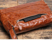 Borsa a tracolla in pelle marrone su tavolo in legno, con cerniera frontale e tracolla regolabile. Accessorio moda elegante e pratico.