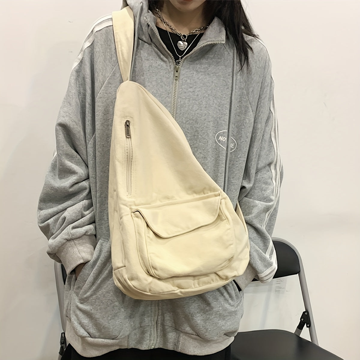 Donna con felpa grigia oversize e borsa a tracolla beige. Stile casual, moda urbana, abbigliamento comodo. Accessorio pratico e versatile.