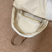 Zaino beige aperto su tappeto marrone, con tasca interna con cerniera. Design elegante e funzionale, ideale per scuola o lavoro.