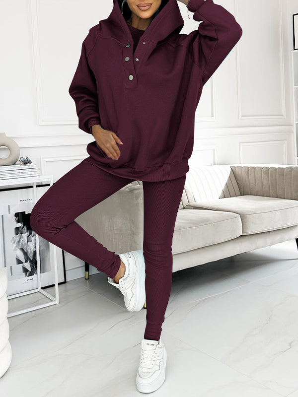 Donna in tuta sportiva bordeaux, felpa con cappuccio e pantaloni aderenti, scarpe da ginnastica bianche, in salotto moderno. Moda casual donna.