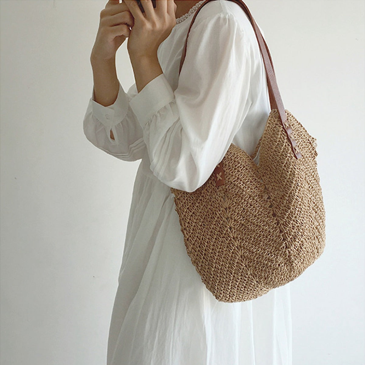 Donna con abito bianco indossa borsa a tracolla in paglia intrecciata, stile boho chic, moda estiva, accessorio casual elegante.
