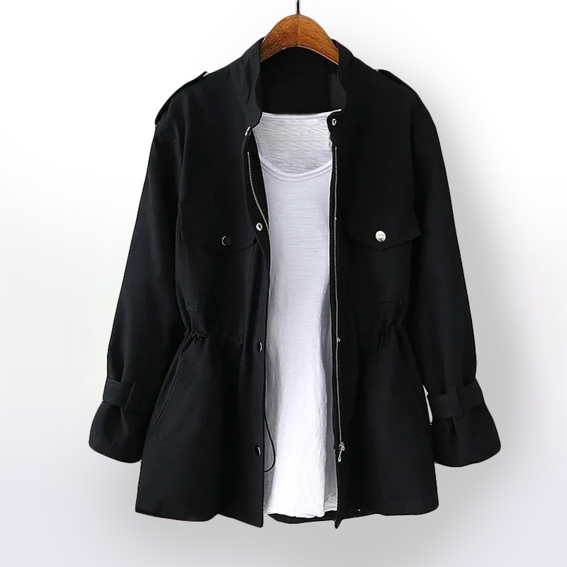 Giacca nera casual da donna con cintura in vita, bottoni argentati e tasche frontali, appesa su gruccia, sopra maglietta bianca. Moda autunnale.