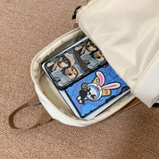 Zaino bianco aperto su tappeto beige con tablet all'interno, copertine con immagini di cani e conigli. Accessori tecnologici, custodie colorate.