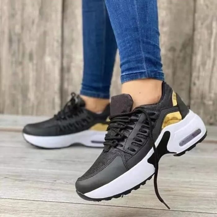 Scarpe da ginnastica nere e oro da donna, suola bianca, indossate con jeans aderenti. Design moderno, casual e sportivo.