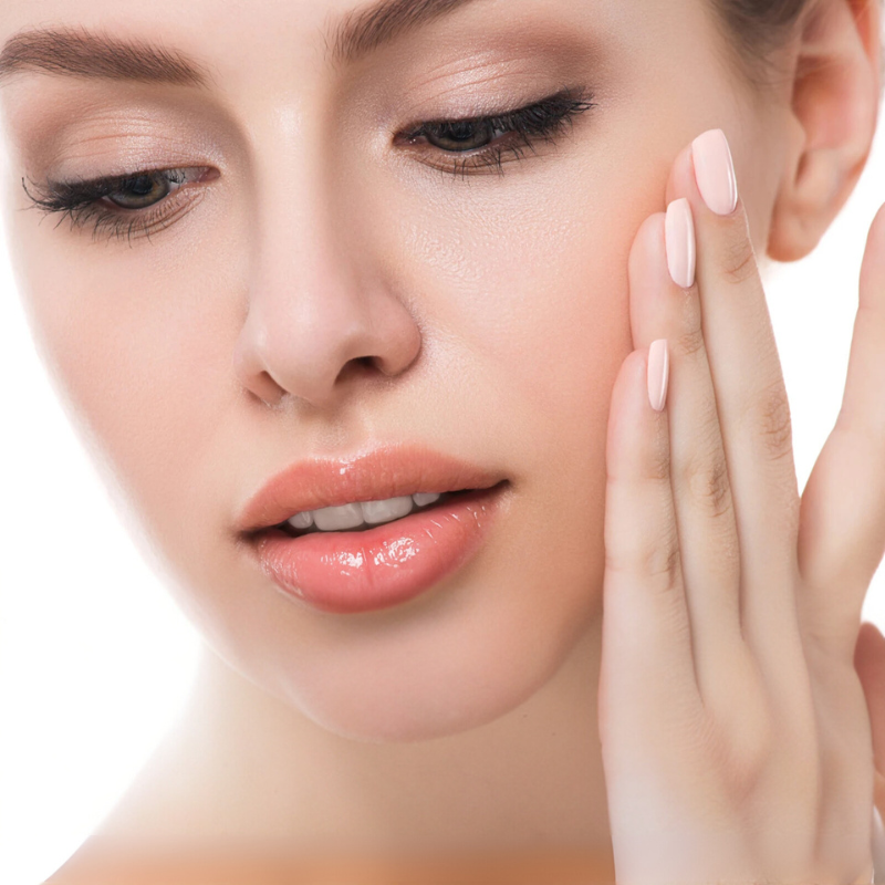 Donna con pelle liscia e trucco naturale, tocca il viso con unghie curate. Bellezza, cura della pelle, trucco leggero, manicure elegante.