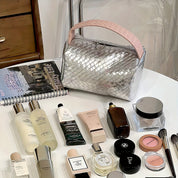 Borsa cosmetica intrecciata argento su tavolo con prodotti di bellezza: creme, profumi, trucco. Accessori moda e bellezza, stile elegante.