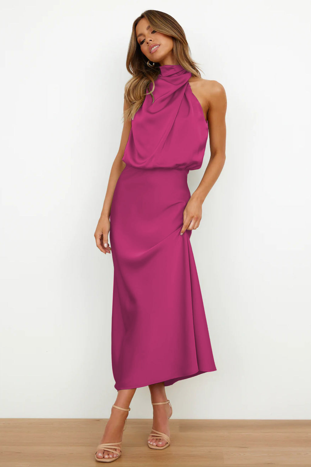 Abito lungo fucsia elegante, senza maniche, con collo alto drappeggiato. Perfetto per eventi formali. Modella in posa su sfondo bianco.