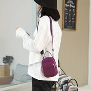 Donna con borsa a tracolla viola, indossa camicia bianca e cappello nero. Moda casual, accessori eleganti, stile urbano.