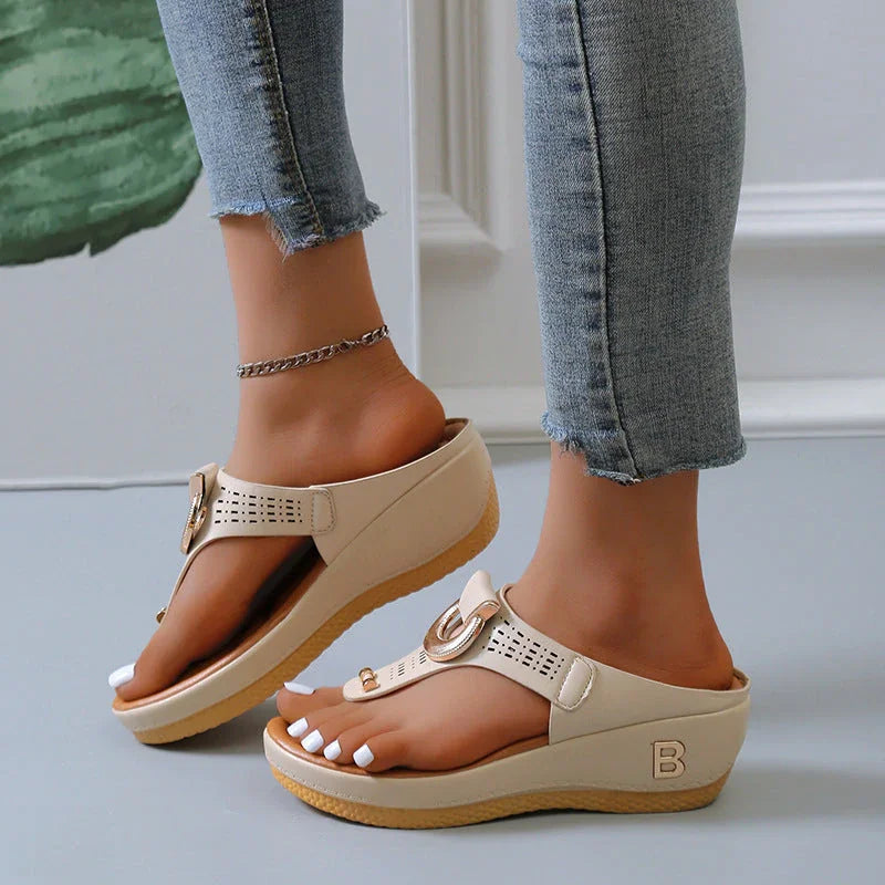 Sandali beige con zeppa, cinturino regolabile e dettagli traforati, indossati con jeans aderenti. Scarpe estive eleganti e comode per donna.