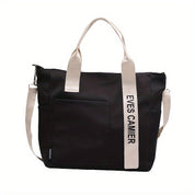 Borsa tote nera con manici bianchi, tasca frontale e scritta "EYES CAMIER". Design moderno, ideale per shopping e uso quotidiano.