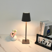 Lampada da tavolo moderna nera su scrivania con fiori in vaso, libri e calendario. Design elegante per arredamento casa e ufficio.