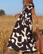 Donna in abito lungo estivo con motivo geometrico bianco e nero, in un campo di grano. Moda femminile, abbigliamento estivo elegante.