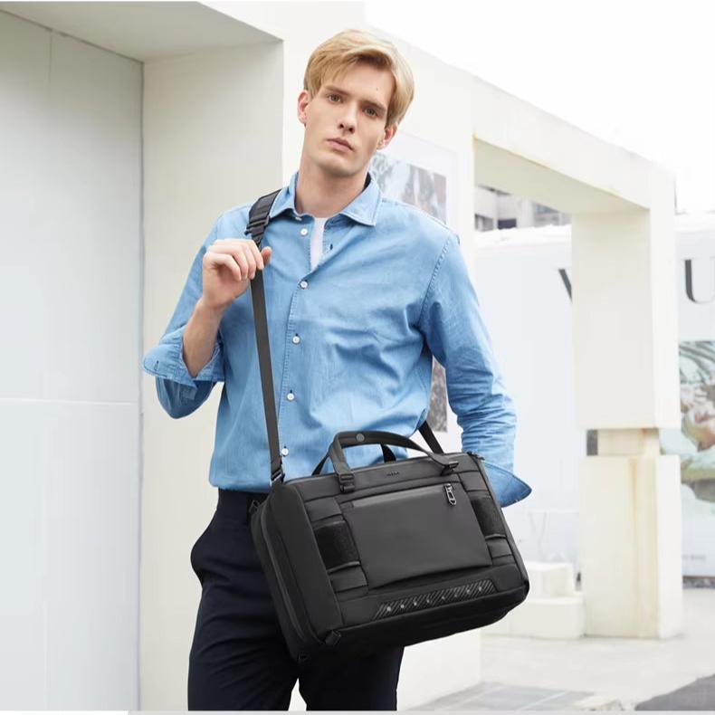 Uomo con camicia azzurra indossa borsa a tracolla nera elegante, ideale per lavoro e viaggi. Design moderno, pratico e spazioso.