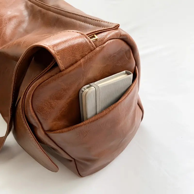 Zaino in pelle marrone con tasca frontale contenente un taccuino. Design elegante, ideale per viaggi e lavoro. Accessorio moda versatile.