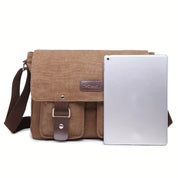 Borsa a tracolla in tela marrone con patta, tasche frontali e cinturino regolabile, accanto a tablet argento. Ideale per lavoro e viaggio.