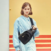 Donna con giacca azzurra indossa borsa a tracolla nera elegante, sfondo giallo e rosso. Moda femminile, accessori trendy, stile urbano.