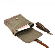 Borsa a tracolla in tela cerata verde con chiusura a bottone, tasca interna, tracolla regolabile marrone e dettagli in pelle. Perfetta per uomo e donna.