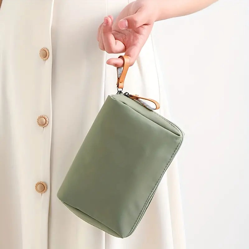 Donna con borsa a mano verde salvia, design minimalista, chiusura a zip, manico in pelle marrone. Accessorio moda elegante e versatile.