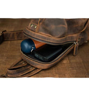 Zaino in pelle marrone con cerniera aperta, mostra power bank nero e oggetto blu all'interno. Accessori moda, zaino vintage, stile retrò.