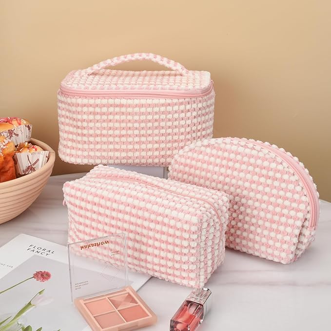 Set di tre beauty case rosa a quadretti, con cerniera, su tavolo bianco. Include borsa trucco, organizer cosmetici, accessori viaggio.