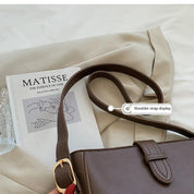 Borsa a tracolla marrone su rivista d'arte Matisse, con fibbia dorata, su sfondo beige. Accessorio moda elegante e versatile.