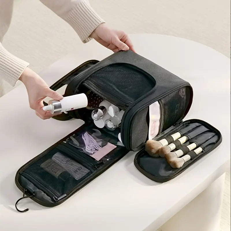 Borsa da viaggio per cosmetici nera con scomparti aperti, contenente pennelli trucco e flaconi. Ideale per organizzare prodotti di bellezza.