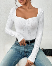 Donna con top bianco traforato a maniche lunghe e jeans blu, seduta su sfondo bianco. Moda casual elegante, abbigliamento femminile trendy.