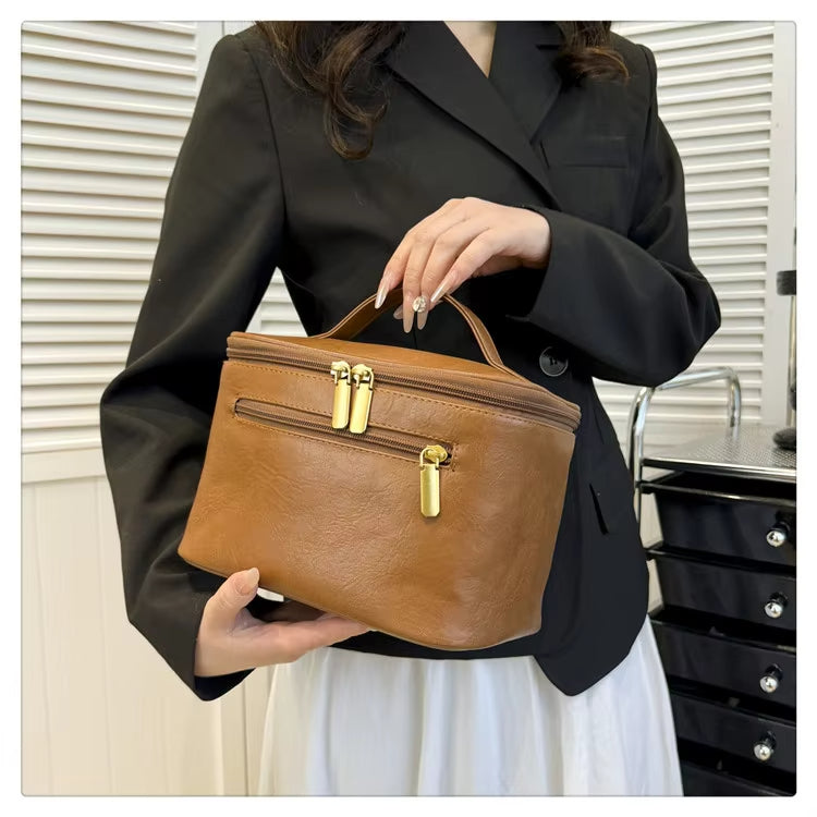 Borsa a mano in pelle marrone con doppia zip dorata, indossata da una donna in giacca nera. Elegante accessorio moda femminile.