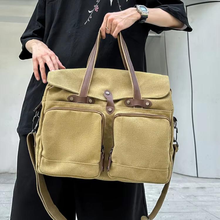 Borsa a tracolla in tela beige con manici in pelle marrone, tasche frontali con cerniera, indossata da una persona in abbigliamento casual.