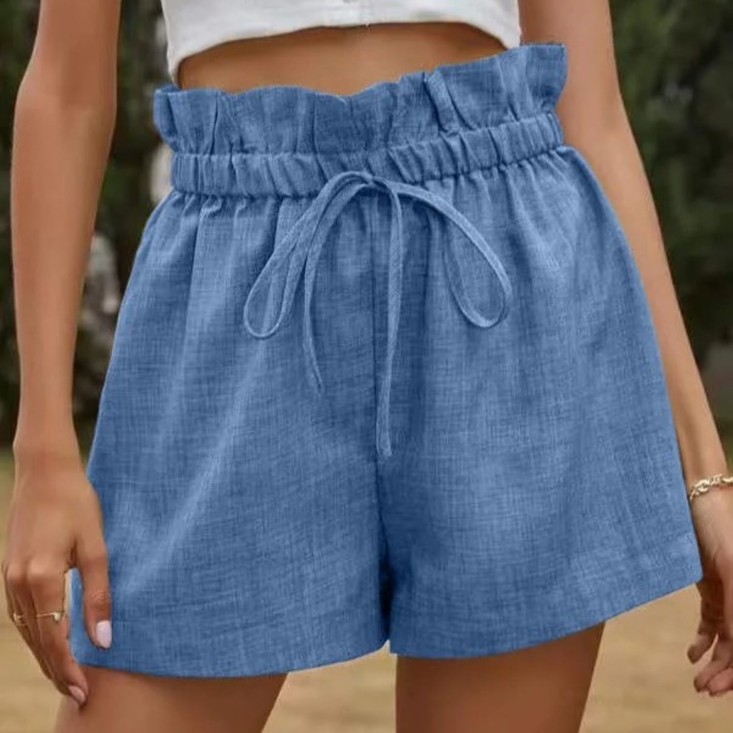 Shorts a vita alta in denim blu con cintura arricciata e laccio, indossati da una donna. Stile casual estivo, moda femminile trendy.