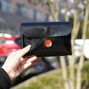 Portafoglio in pelle nera con bottone rosso, tenuto in mano all'aperto. Design elegante, accessorio moda, ideale per uomo e donna.