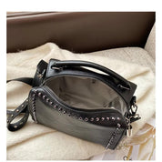 Borsa a tracolla in pelle nera con borchie argentate, cerniera aperta, manico superiore e tracolla regolabile, su sfondo chiaro.