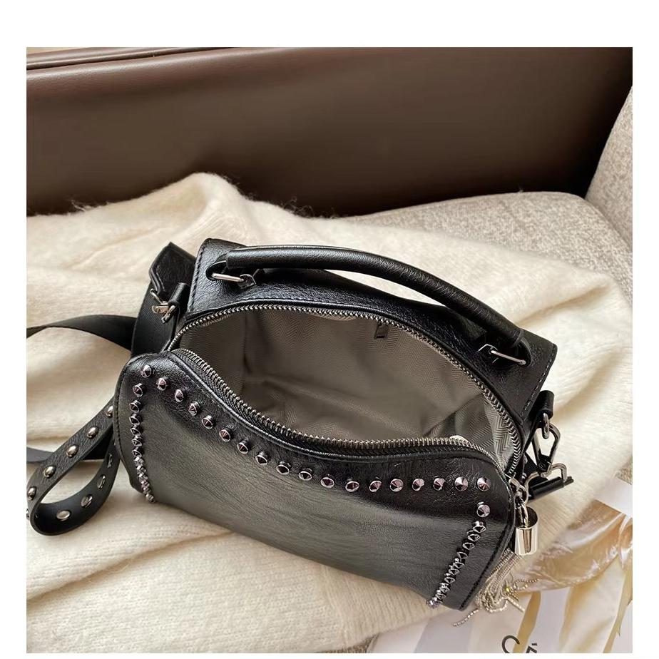 Borsa a tracolla in pelle nera con borchie argentate, cerniera aperta, manico superiore e tracolla regolabile, su sfondo chiaro.