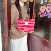 Donna con maglione marrone tiene una borsa a righe rosse e rosa, davanti a una porta con adesivi. Accessorio moda invernale, stile casual.