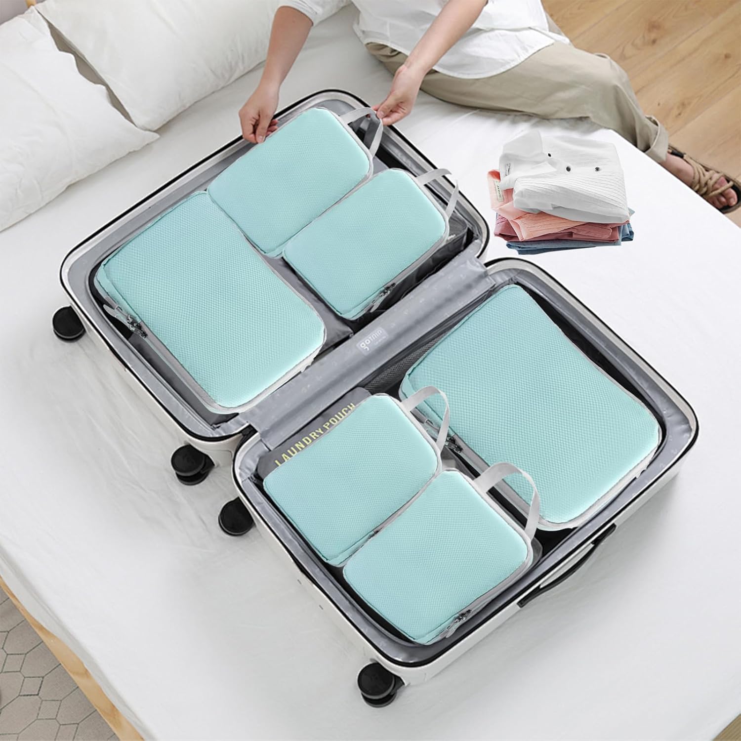 Valigia aperta su letto con organizer da viaggio azzurri, abbigliamento piegato accanto. Ottimizza spazio, ideale per viaggi organizzati.