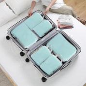 Valigia aperta su letto con organizer da viaggio azzurri, abbigliamento piegato accanto. Ottimizza spazio, ideale per viaggi organizzati.