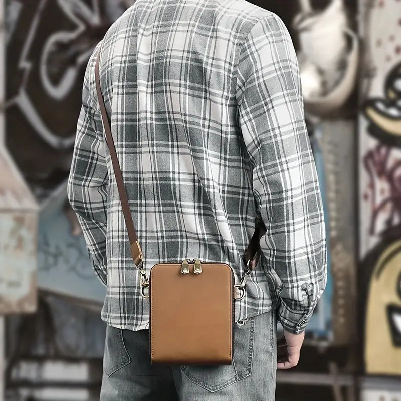Uomo con camicia a quadri e jeans indossa borsa a tracolla in pelle marrone, stile casual urbano. Accessorio moda maschile, street style.