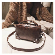 Borsa a tracolla in pelle marrone su letto, design rettangolare con manico superiore e dettagli metallici. Accessorio moda elegante per donna.