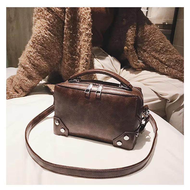 Borsa a tracolla in pelle marrone su letto, design rettangolare con manico superiore e dettagli metallici. Accessorio moda elegante per donna.