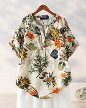 Camicia donna floreale in cotone, maniche corte, sfondo bianco, stampa tropicale colorata, casual estiva, bottoni frontali, appesa su gruccia.