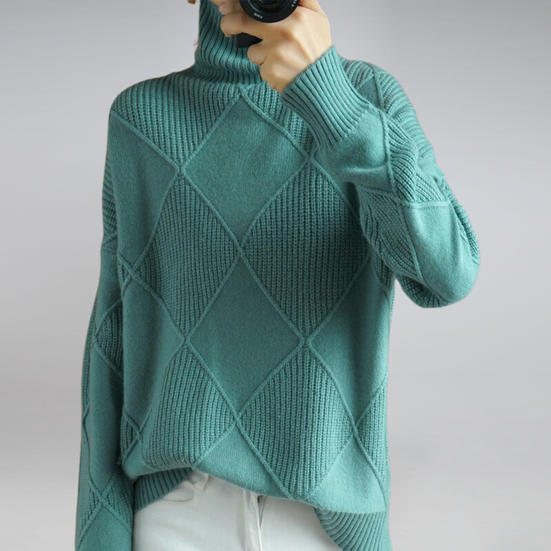 Maglione verde acqua a collo alto con motivo a rombi, indossato da una persona, abbinato a pantaloni bianchi. Moda autunnale elegante e casual.